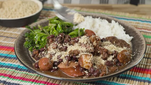 Sprinkling farofa over feijoada. A complete Brazilian feast including rice and kale. Farofa is a Brazilian fried flour that is a popular side dish in Brazil.