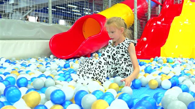Cute little girl playing and throwing plastic balls in colorful dry ball pit at indoor playground