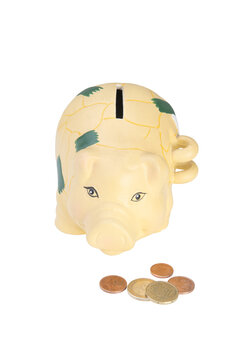 A yellow piggy bank with green markings sits next to a few euro coins