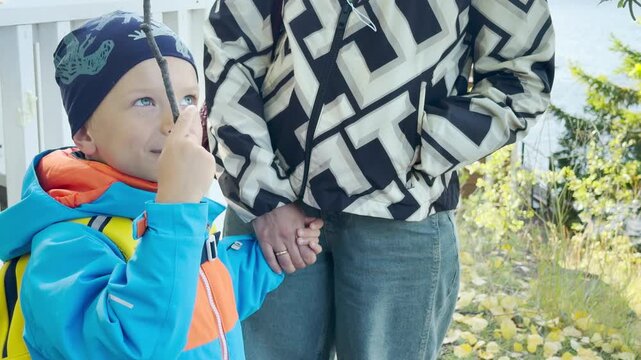 A little boy holds a stick while standing with his mother at Valaam near Lake Ladoga. They enjoy a pleasant outdoor stroll together. The moment fills them with cheerful wonder and warm family love.