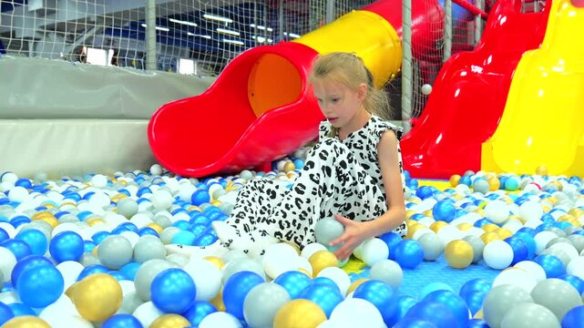 Cute little girl playing and throwing plastic balls in colorful dry ball pit at indoor playground
