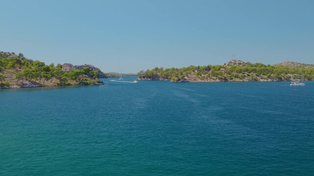 Aerial drone footage flying forward over Luka Channel near &Scaron;ibenik, Croatia, revealing turquoise waters, multiple boats and wakes, rocky shores, lush Mediterranean islands and scenic coastline.