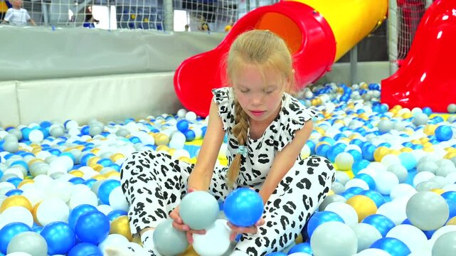 Cute little girl playing and throwing plastic balls in colorful dry ball pit at indoor playground