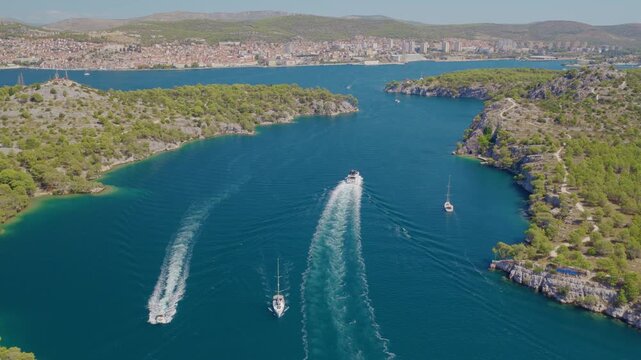 Aerial drone footage flying forward over Luka Channel near &Scaron;ibenik, Croatia, revealing turquoise waters, multiple boats and wakes, rocky shores, lush Mediterranean islands and scenic coastline.