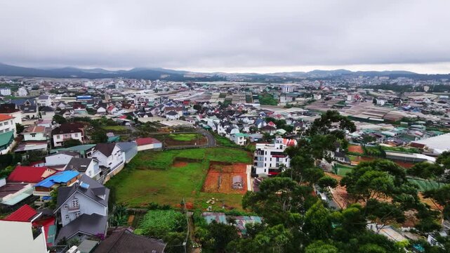Aerial tracking shot of cityscape with green fields and cloudy sky during daytime