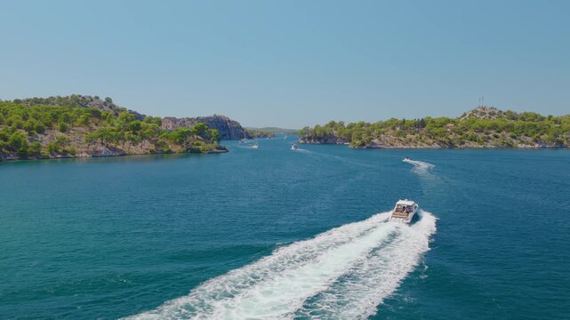 Aerial drone footage over Luka Channel near &Scaron;ibenik, Croatia, tracking a fast motorboat as it speeds across the blue Adriatic waters, leaving a dramatic white wake among rocky, pine-covered islands.
