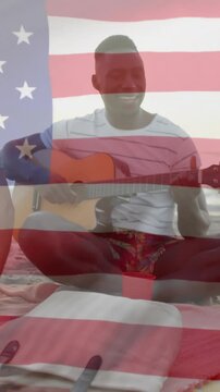 Animation of american flag over happy diverse friends playing guitar and singing on sunny beach