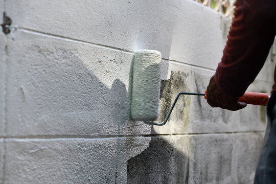 Paint roller applying white coating to concrete wall during exterior renovation