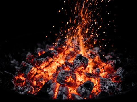 Burning charcoal embers glowing intensely in dark setting