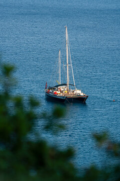 Kotor, Montenegro - 04 July 2005: View of a sailboat anchored in the calm blue waters of the Bay of Kotor, framed by blurred foreground foliage.