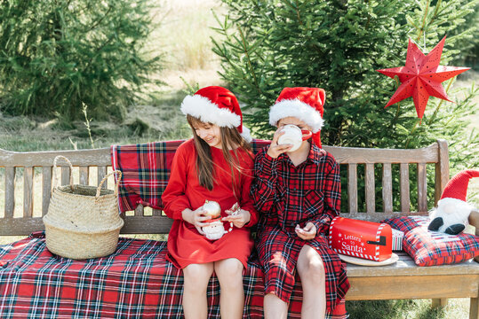 Christmas in July celebration with happy children wearing Santa hats, enjoying festive outdoor setting with Christmas decorations, gifts, evergreen trees and bright summer sunlight.