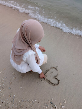Woman drawing heart shape on a sand beach