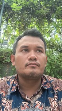 Portrait of a middle age southeast Asian man wearing a traditional batik shirt outdoors.
