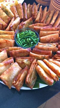 Vertical zoom out reveal of traditional Indonesian martabak mini savory fried rolls with green chilies platter