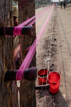 Lahore, Pakistan - 07 February 2026: View of pink kite strings being prepared for the Basant festival, stretched between wooden posts with red dye buckets nearby.