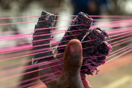 Lahore, Punjab, Pakistan - 07 February 2026: View of a person's hand with fingers wrapped in protective fabric, holding vibrant pink kite strings during the Basant festival.