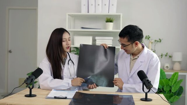 Asian male and female doctors holding an X-ray film, discussing medical diagnosis during a healthcare podcast interview. Recording an educational audio broadcast in a modern clinic studio setting