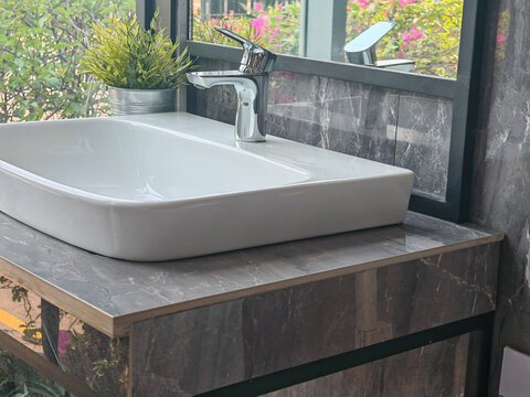 a sleek chrome single-lever faucet mounted on a white ceramic rectangular vessel sink, set against a dark grey marble countertop with a potted green plant and mirror reflection