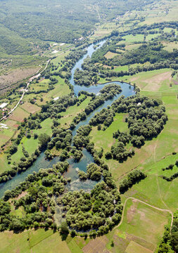 Aerial view of the winding Zeta River flowing through lush green fields and dense vegetation in the rural landscape of Danilovgrad, Danilovgrad Municipal, Montenegro.