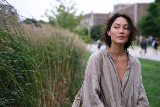 A thoughtful woman stands outdoors, surrounded by tall grass, embodying a natural yet elegant demeanor in a serene and eco-friendly environment.