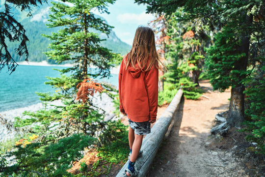 Boy walking along a log railing on a lakeside trail from behind