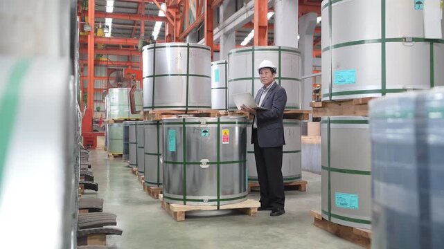 Engineer reviewing metal coil inventory during a quality control audit inside a modern industrial factory warehouse.