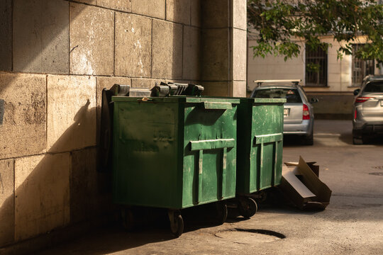 Two empty green trash containers in harsh light