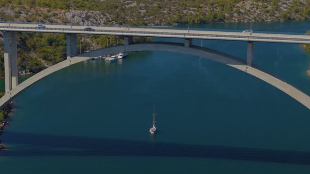 Aerial drone view of Krka Bridge in Croatia, with a smooth orbital camera movement around the concrete bridge above turquoise river waters, rocky landscape and lush Mediterranean vegetation.