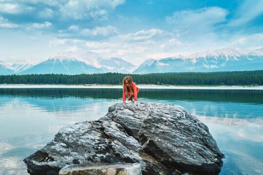 Boy climbing a boulder at a turquoise lake with mountains behind
