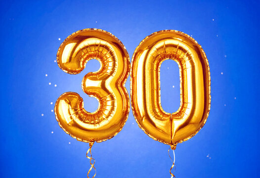 Golden number thirty foil balloons floating against a vibrant blue sky perfect for celebrations and anniversaries