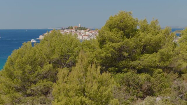 Aerial view of Primo&scaron;ten, Croatia, revealed by a smooth panning camera movement from Mediterranean trees to the historic coastal town, turquoise Adriatic Sea, sailing boats and distant islands.