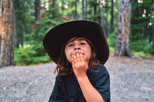 Boy in a cowboy hat with his hand over his mouth at a campsite