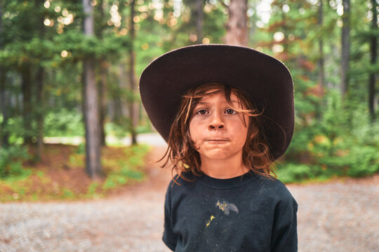 Boy wearing a brown cowboy hat at a forest campsite