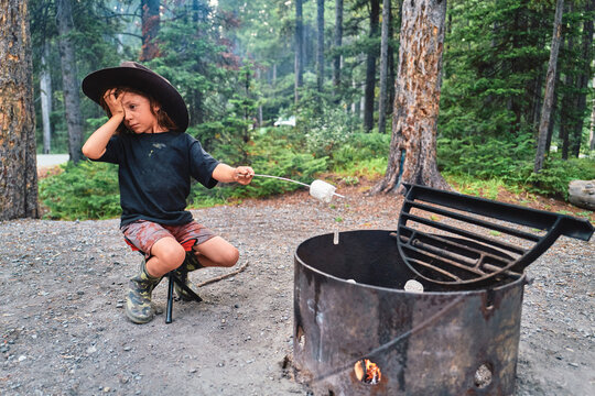 Boy in a cowboy hat roasting a marshmallow over a campfire