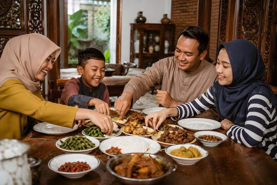 Indonesian family sharing a traditional Nasi Padang meal around a dining table, enjoying rice, rendang, chicken, vegetables, sambal and assorted side dishes together. Warm lighting and candid expressi