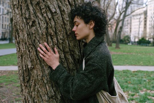 A young person leans gently against a textured tree trunk, symbolizing the harmony between youth and nature, fostering emotional tranquility and self-discovery in an urban setting.