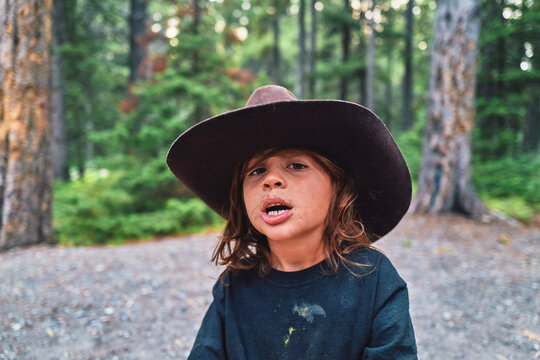 Boy in a cowboy hat with mouth open at a forest campsite
