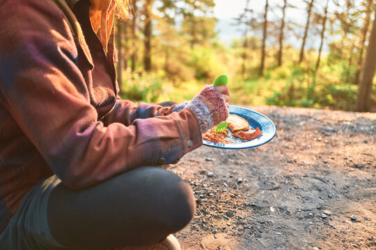 woman eating breakfast at a campsite with golden forest light behind