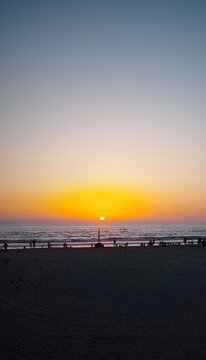 Silhouetted beachgoers watching the sun set over the ocean horizon