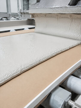 Gypsum slurry pouring onto paper liner on conveyor belt during drywall board manufacturing. Industrial production of plasterboard for construction and interior finishing