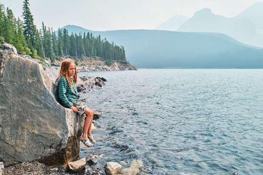 Boy sitting on the edge of a boulder at a mountain lake with forest behind