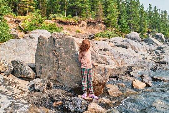 Boy standing beside a large boulder on a rocky lakeshore from behind