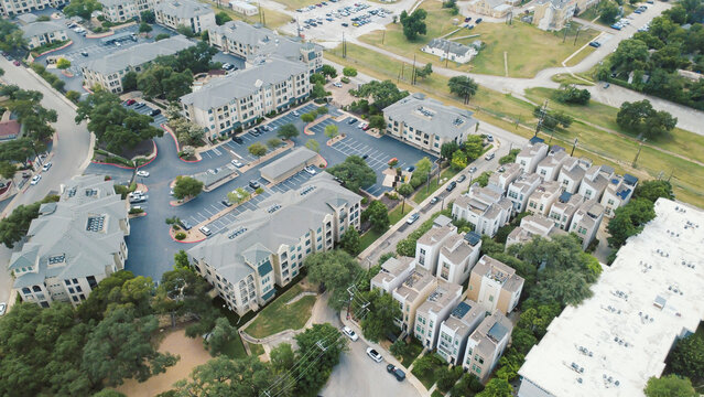 Modern multi tier townhomes anchor Mahncke Park near Broadway corridor. Geometric building rooftops frame private vehicle parking bays, lush tree clusters, San Antonio, Texas