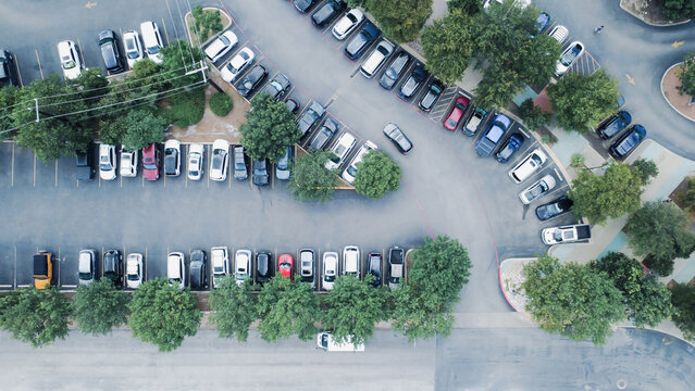 Paved asphalt parking stalls serve commercial facilities near Broadway. Parallel rows of parked vehicles border manicured green medians, pedestrian walkways, San Antonio, Texas