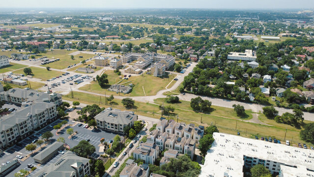 Multi family complexes flank open green spaces near Broadway corridor. Terraced residential rooftops overlook spacious surface lots, landscaped medians, quiet streets, San Antonio, Texas
