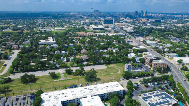 Observation tower rises beyond Broadway Mahncke Park tree canopy. Rooftop solar panels border dense neighborhood greenery, multi family residences, open green lawns, San Antonio, Texas