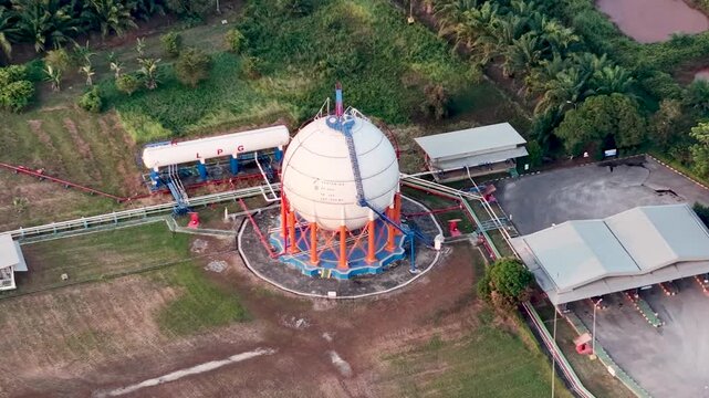 Aerial view of a white spherical industrial gas container surrounded by green vegetation and trees