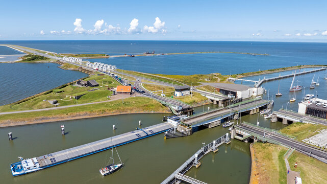 Aerial view of the Afsluitdijk causeway featuring sluice gates, a bridge over the waterway with boats, and green embankments in Breezanddijk, Friesland, Netherlands.
