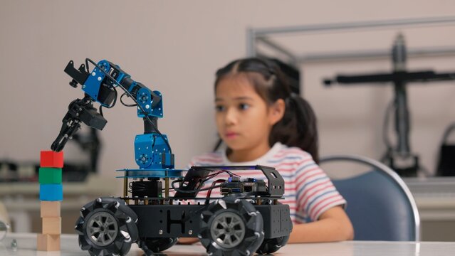Asian girl student programming robotic arm car with digital tablet in STEM classroom. Science technology engineering mathematics education, creative robotics coding and smart school concept.