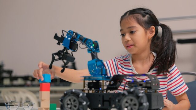 Asian girl student programming robotic arm car with digital tablet in STEM classroom. Science technology engineering mathematics education, creative robotics coding and smart school concept.